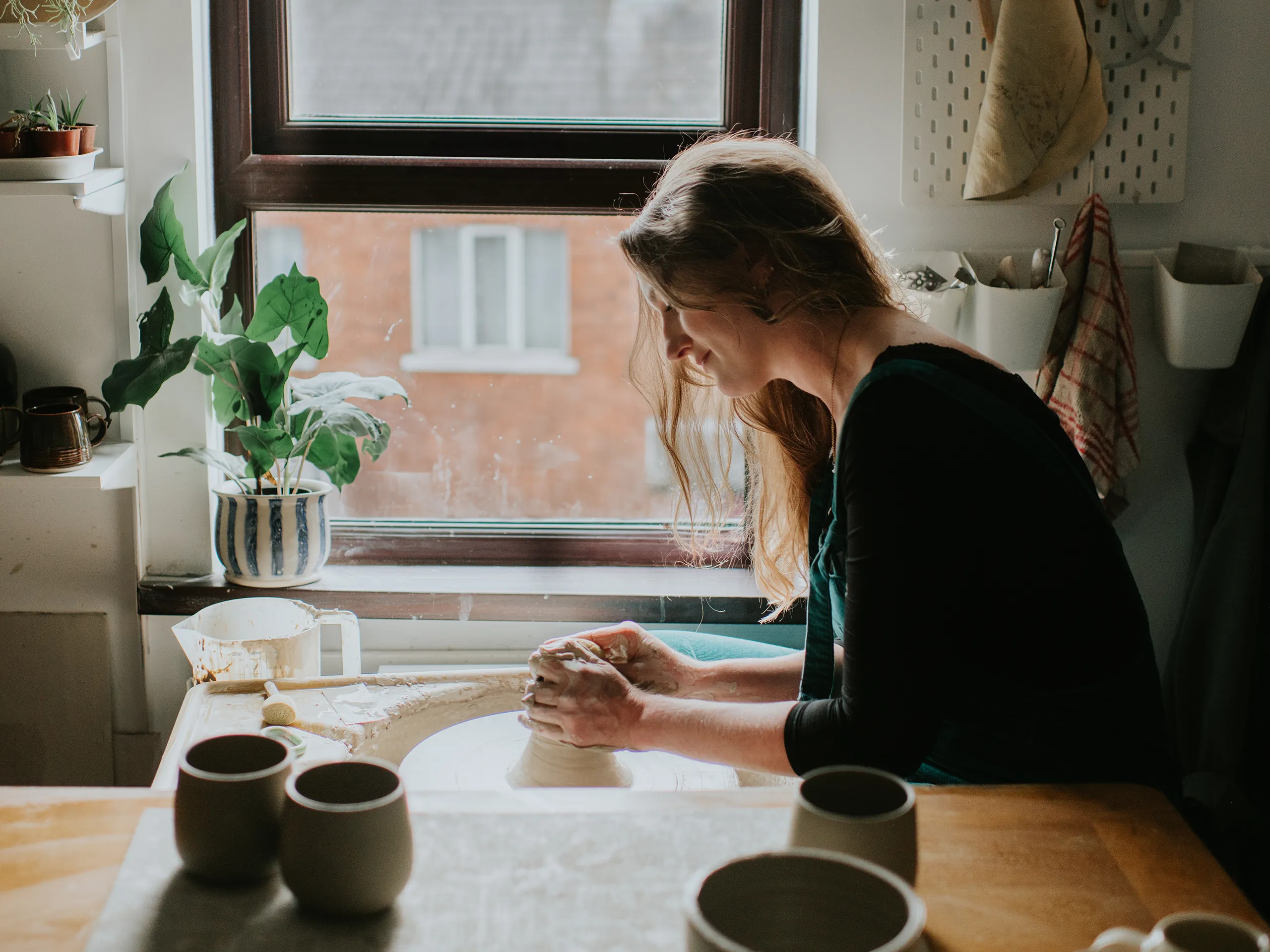 Frau arbeitet an einer Töpferscheibe in ihrem Atelier vor einem Fenster