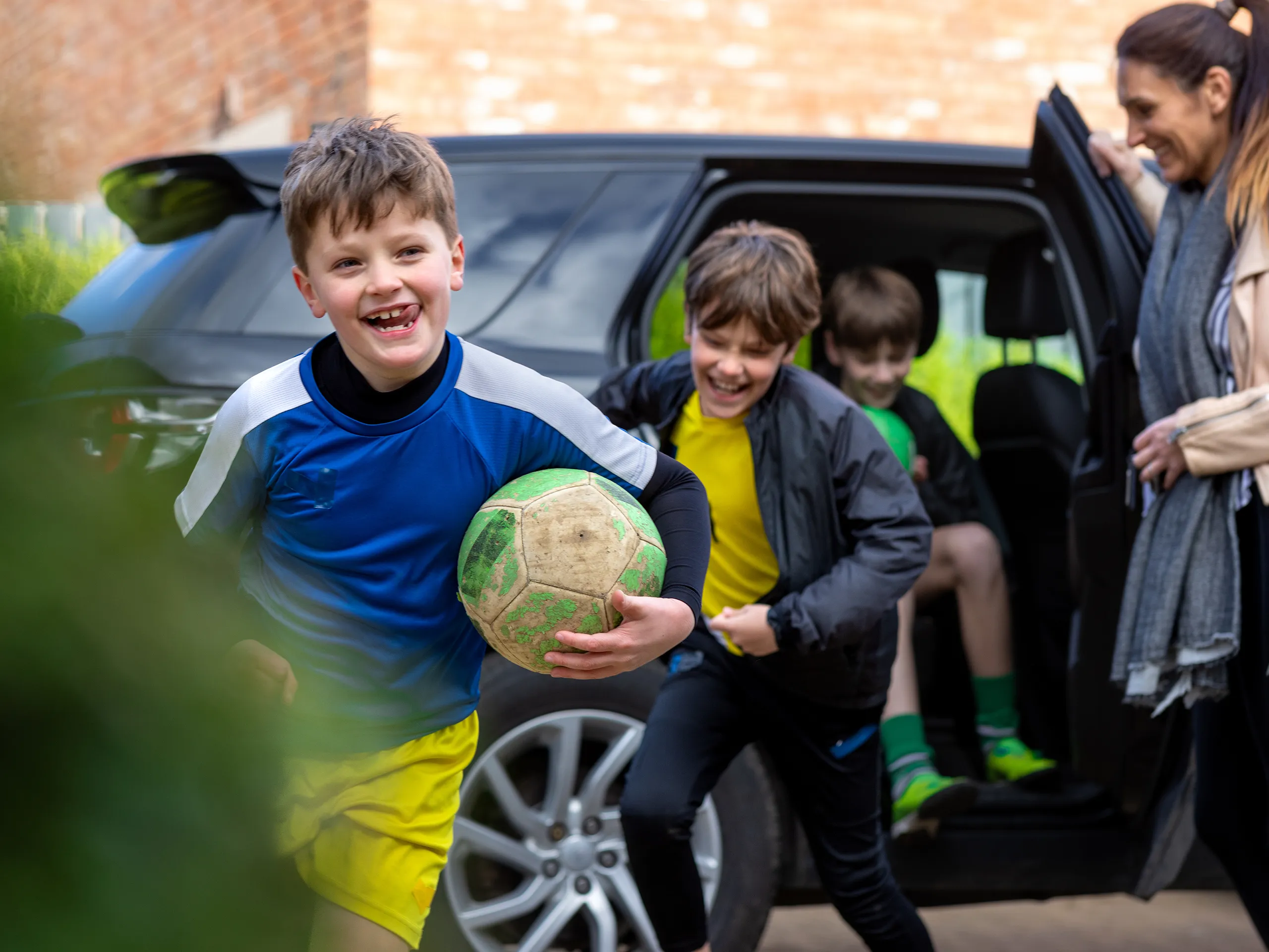 Lachende Kinder steigen aus dem Auto und rennen mit einem Fußball los.
