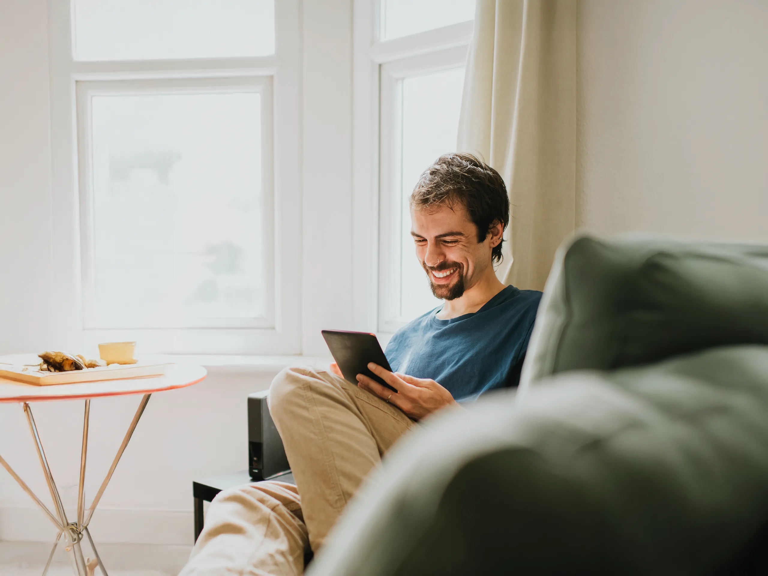 Mann liest entspannt auf Tablet im Wohnzimmer
