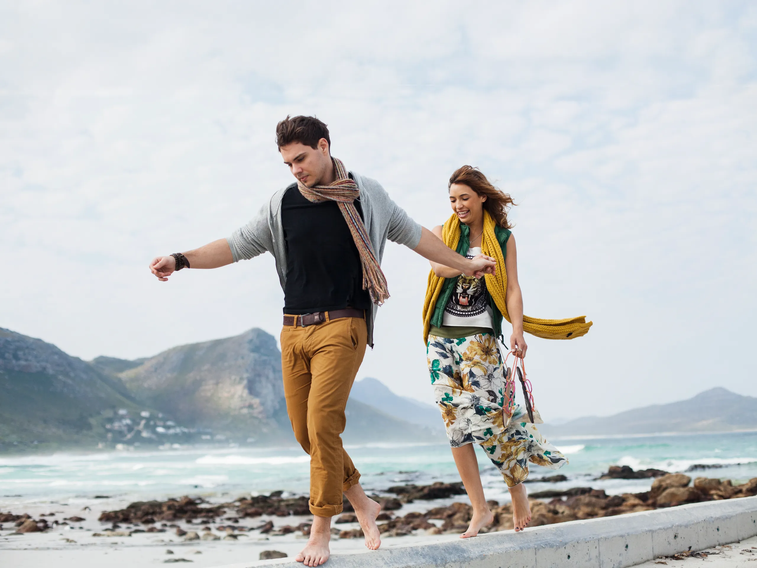 Lächelndes Paar spaziert barfuß am Strand und hält Händchen.