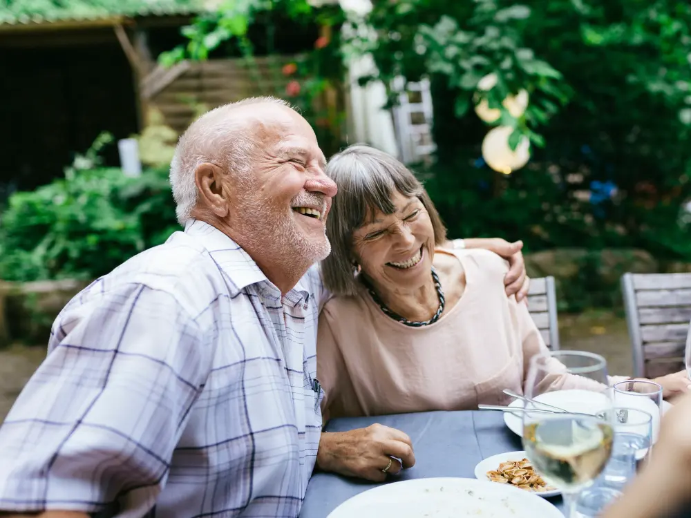 Älteres Paar lacht herzlich beim Essen im Garten
