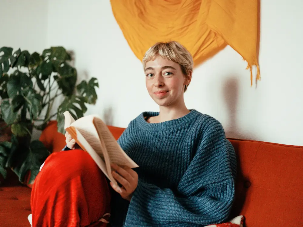 Frau mit blauem Pullover sitzt auf einem Sofa und liest ein Buch