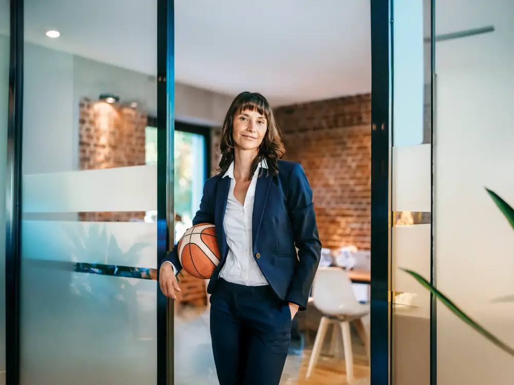 Frau im Business-Anzug hält einen Basketball in einem modernen Büro.