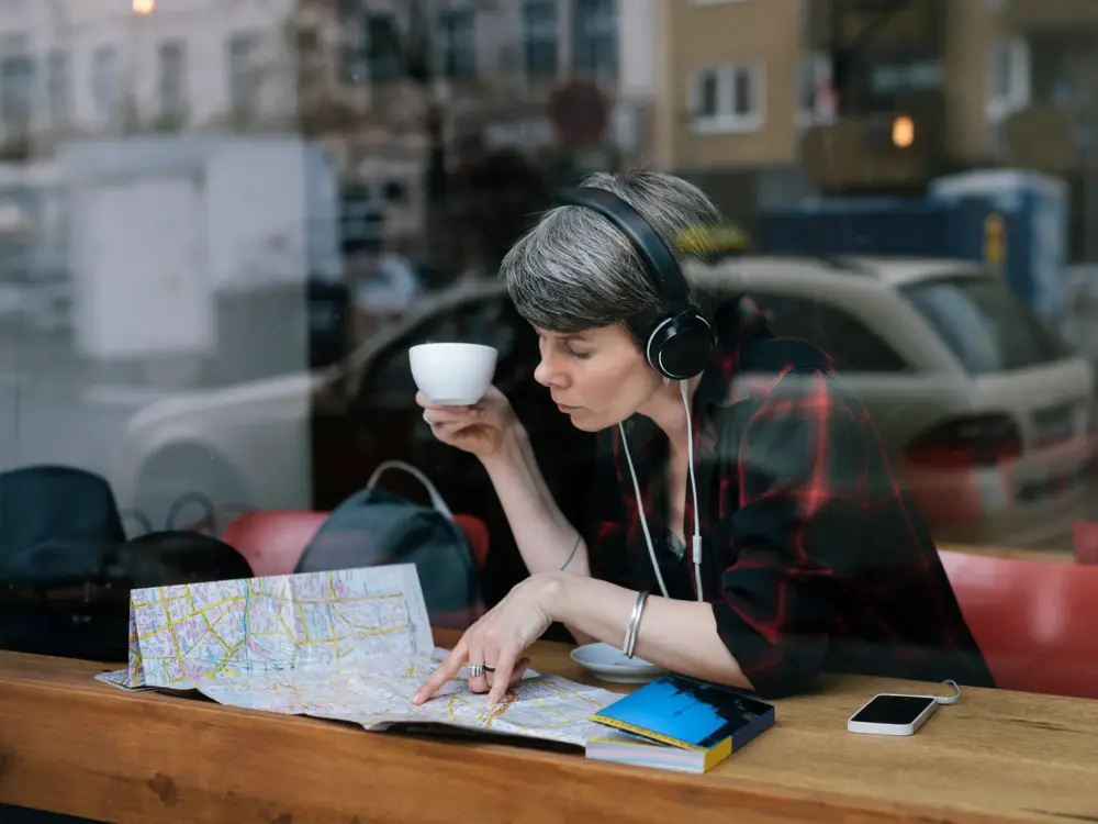 Frau mit Kopfhörern trinkt Kaffee und studiert eine Landkarte in einem Café.