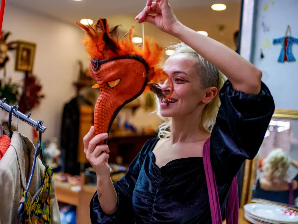 Lächelnde Frau hält eine rote Drachenmaske vor ihr Gesicht in einem Vintage-Laden.