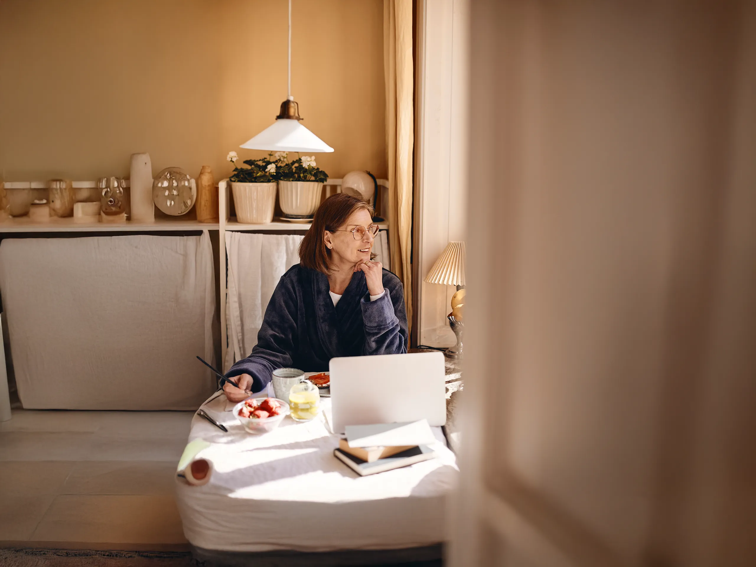 Frau frühstückt im Bademantel und arbeitet am Laptop zu Hause