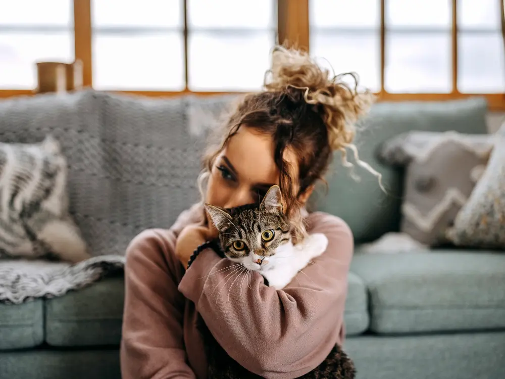 Frau umarmt liebevoll ihre Katze in einem gemütlichen Wohnzimmer.