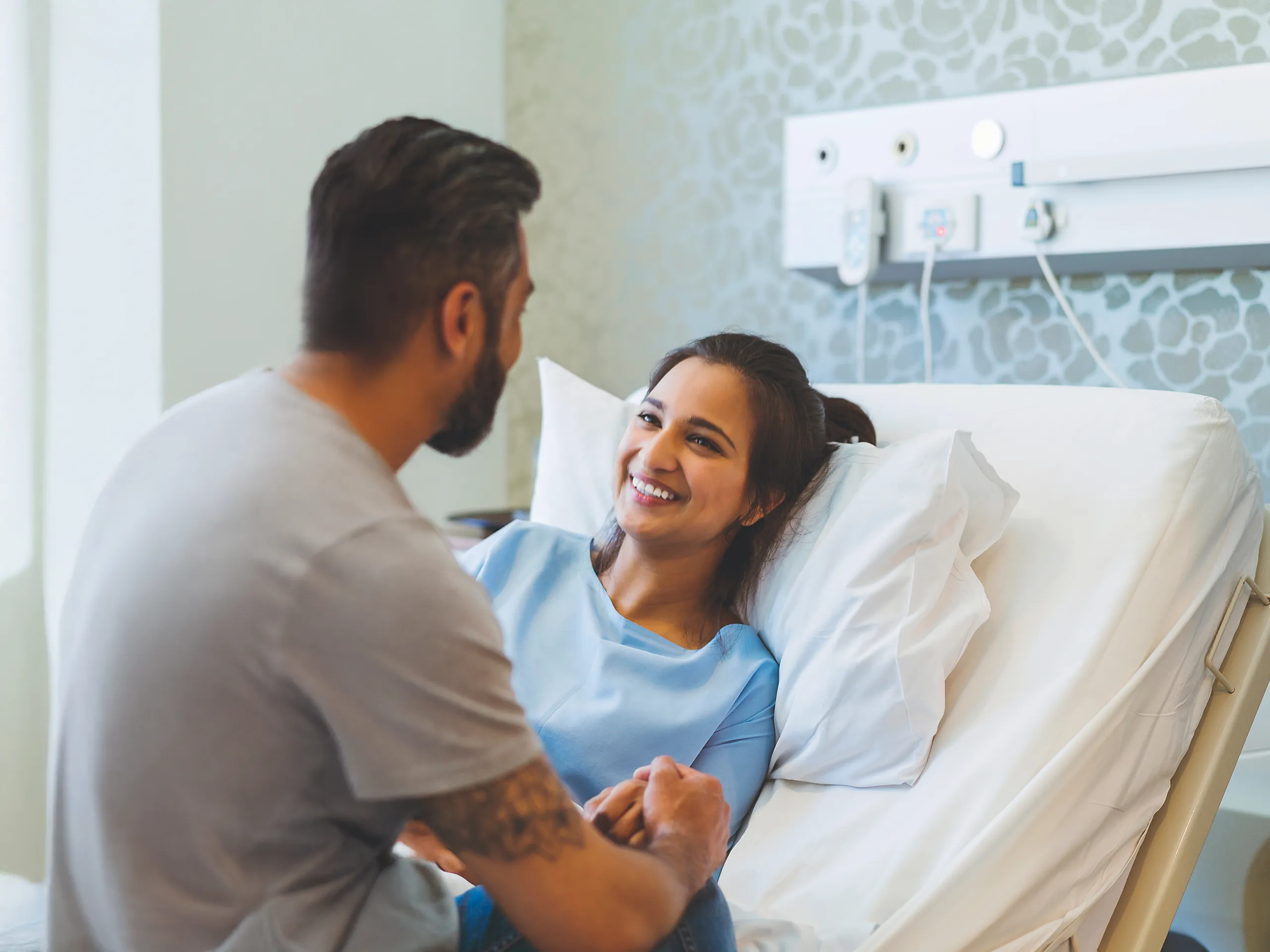 Lächelnde Frau im Krankenhausbett hält die Hand eines Mannes
