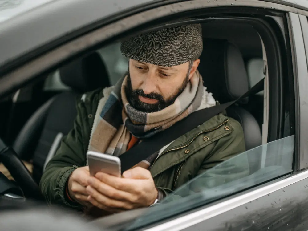 Mann im Auto, der auf seinem Smartphone tippt, während er den Sicherheitsgurt trägt