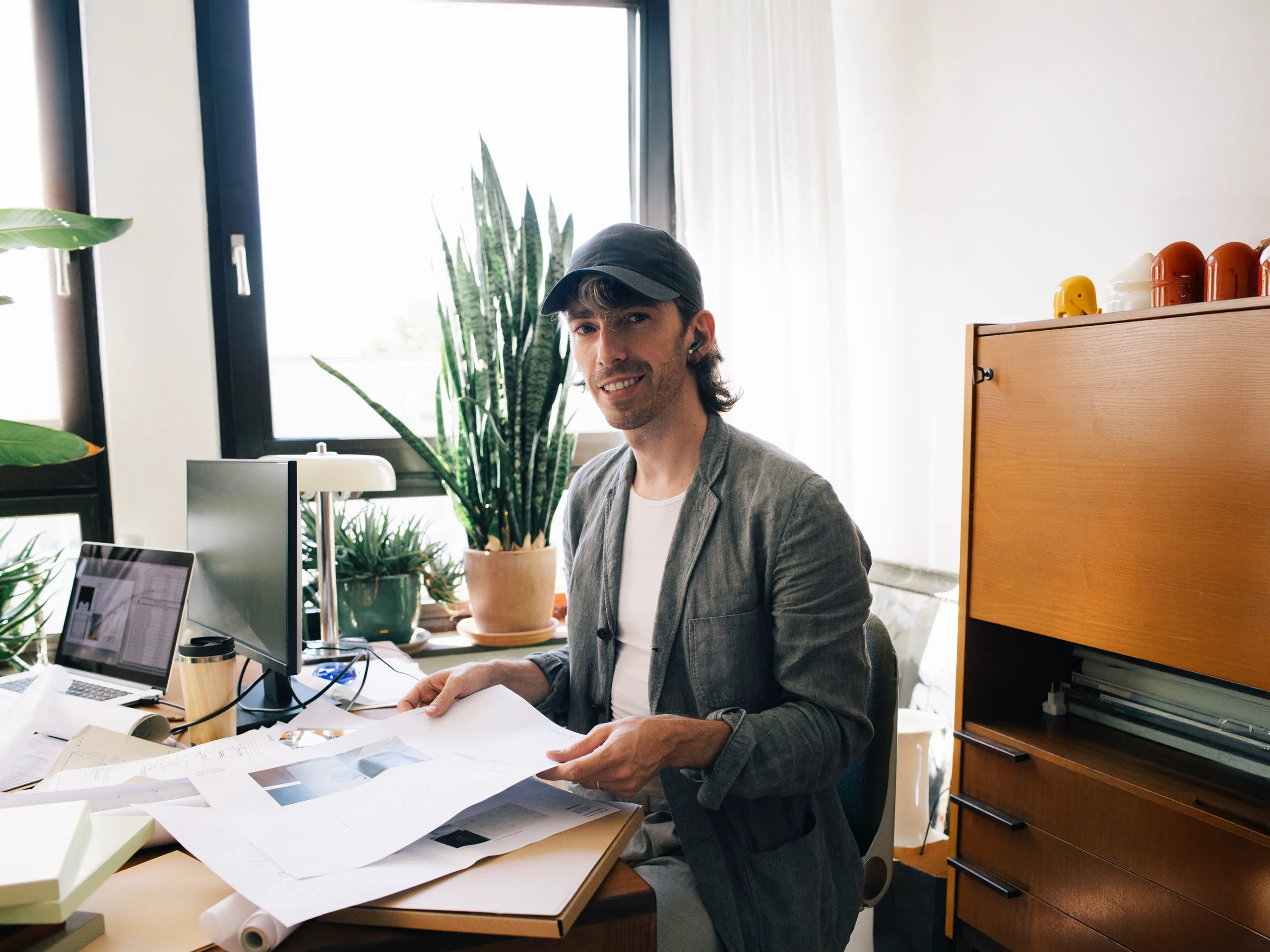 Mann mit Basecap arbeitet an Schreibtisch mit vielen Pflanzen