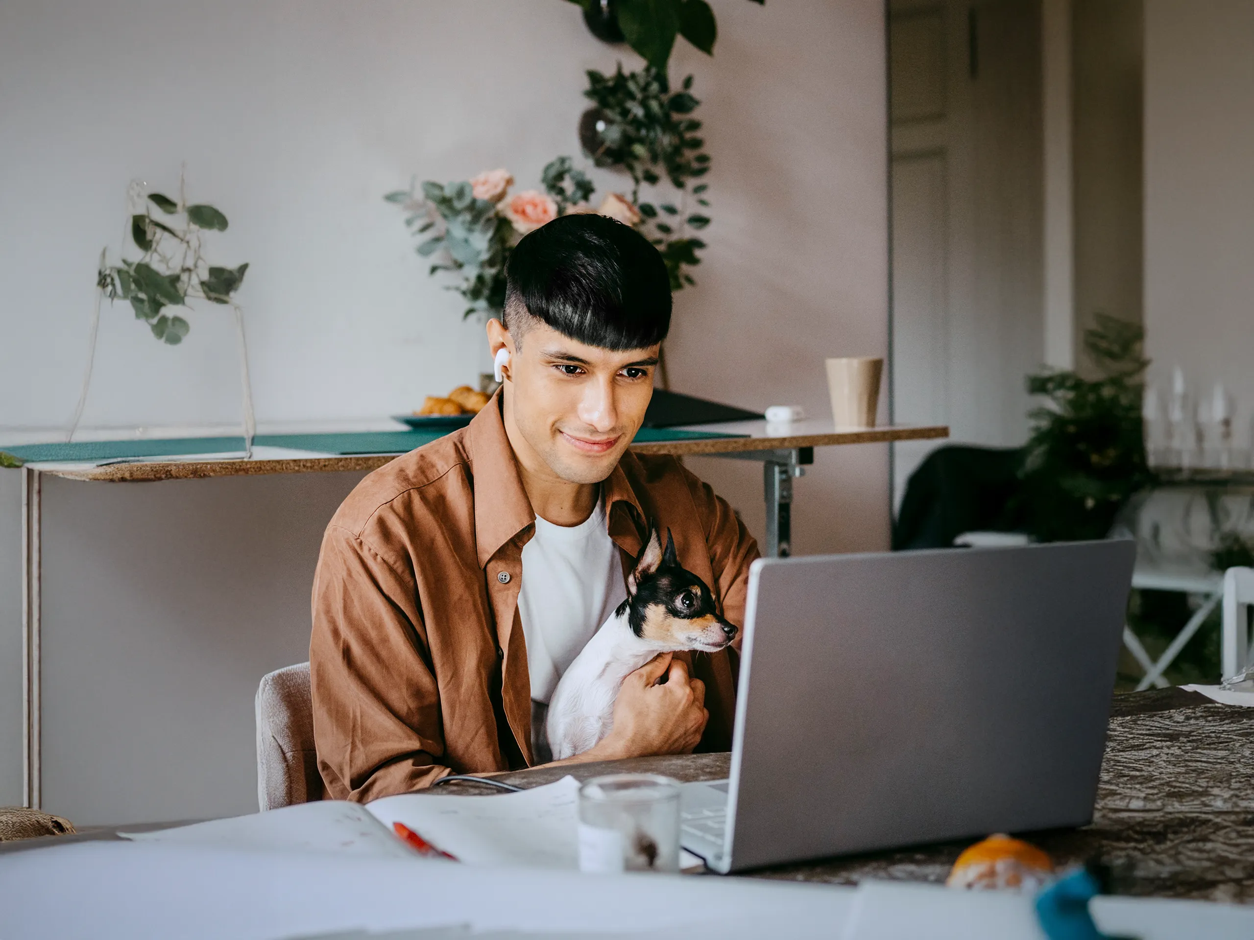 Mann arbeitet mit Laptop und kleinem Hund im Arm