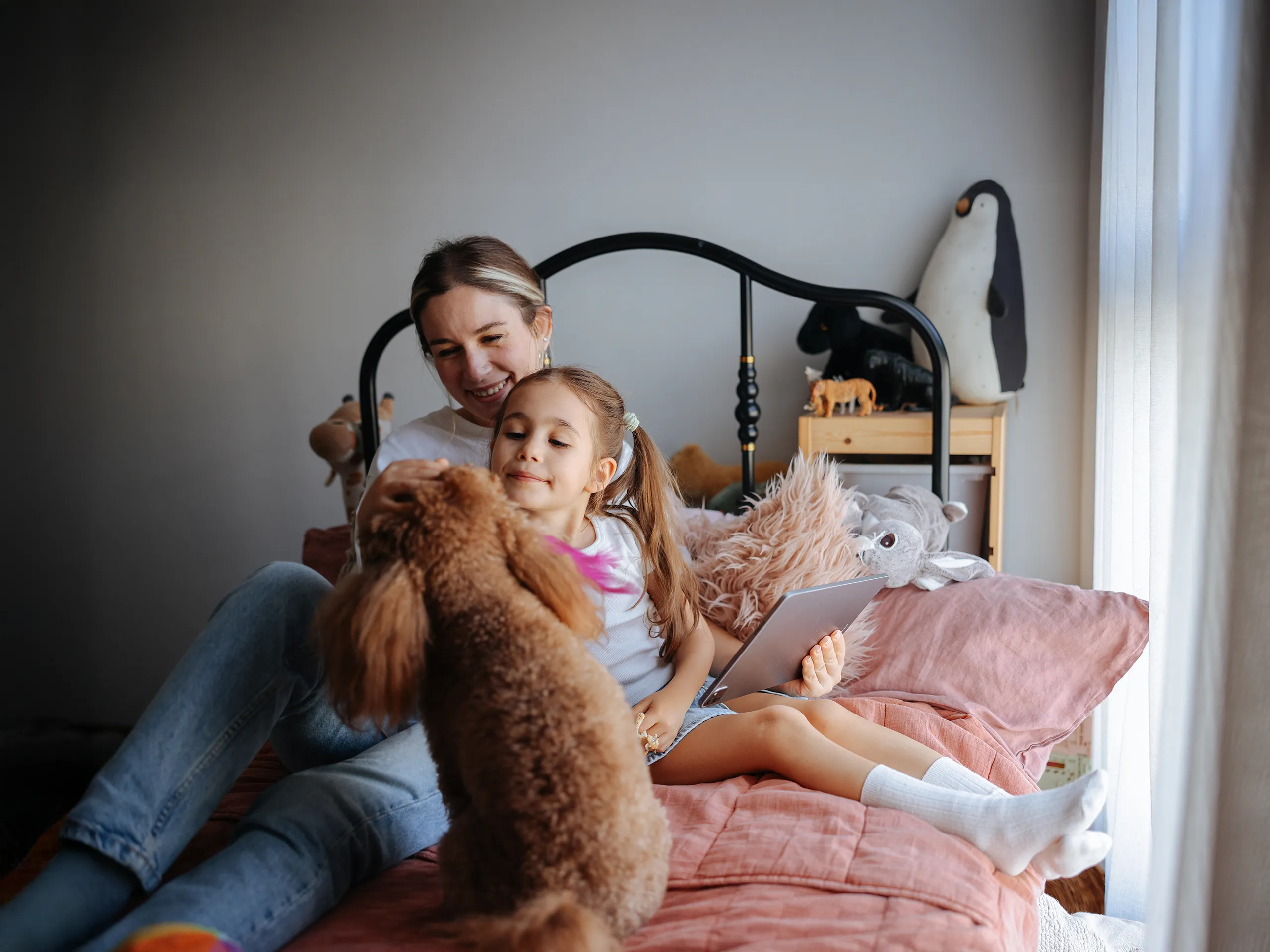 Mutter und Tochter mit Tablet spielen mit Hund auf dem Bett