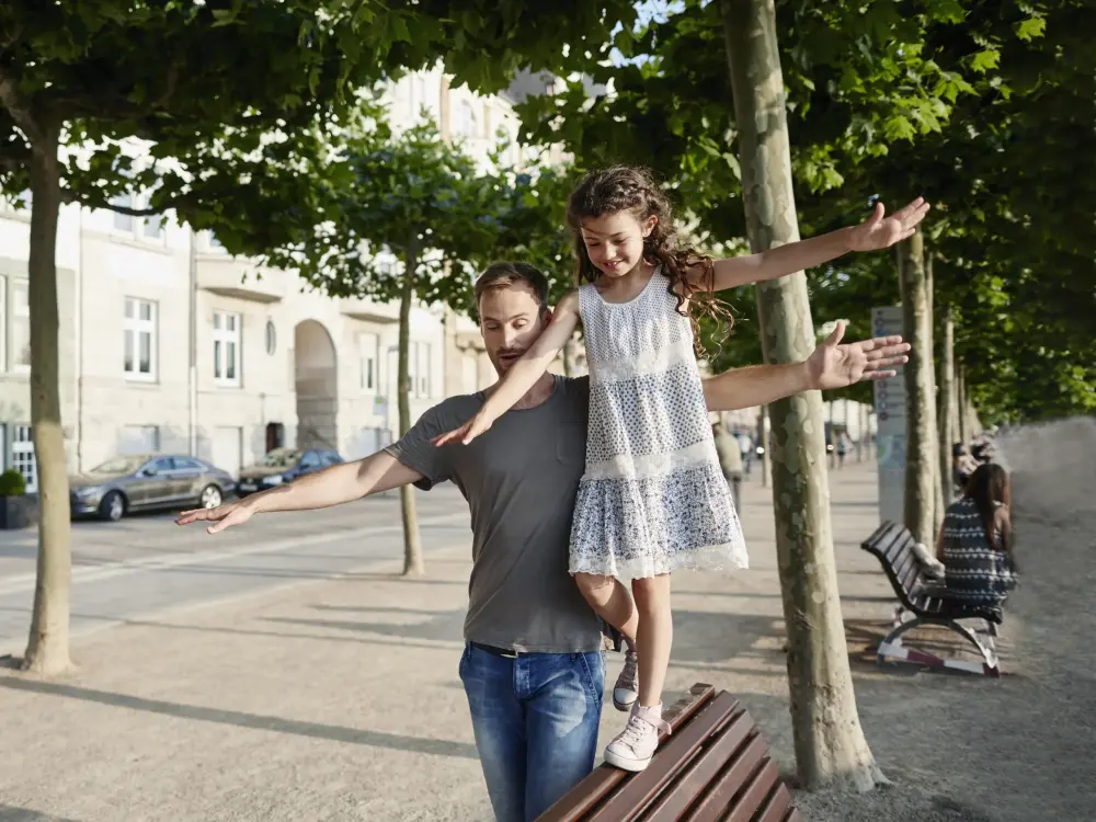 Vater balanciert Tochter im Sommer auf Parkbank