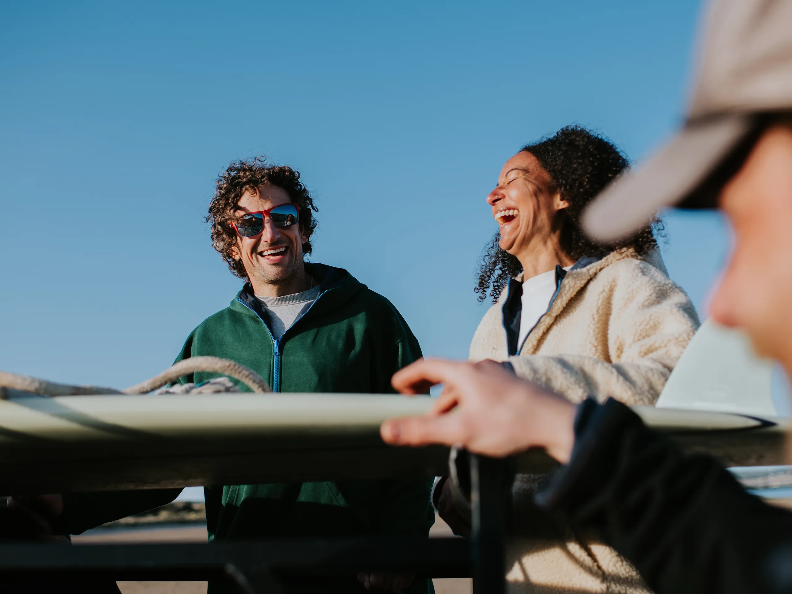 wei Menschen lachen gemeinsam am Strand neben einem Surfbrett